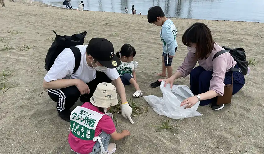 ゴミを拾う組合員の家族ら（５月27日、田ノ浦ビーチ）提供写真