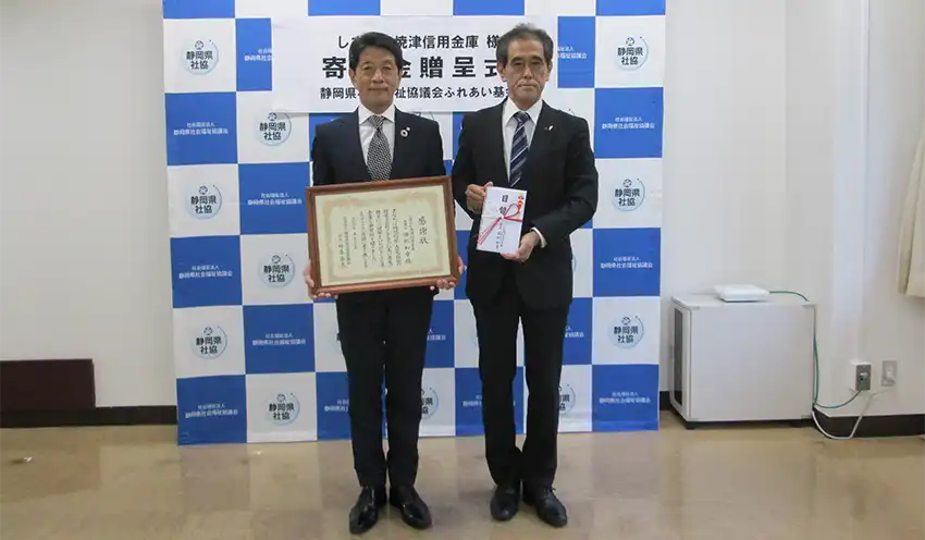 岩﨑浩季・しずおか焼津信金常務理事（左）から藤原学・社会福祉協議会常務理事に目録が贈られた（5月27日、静岡県総合社会福祉会館、しずおか焼津信金提供）