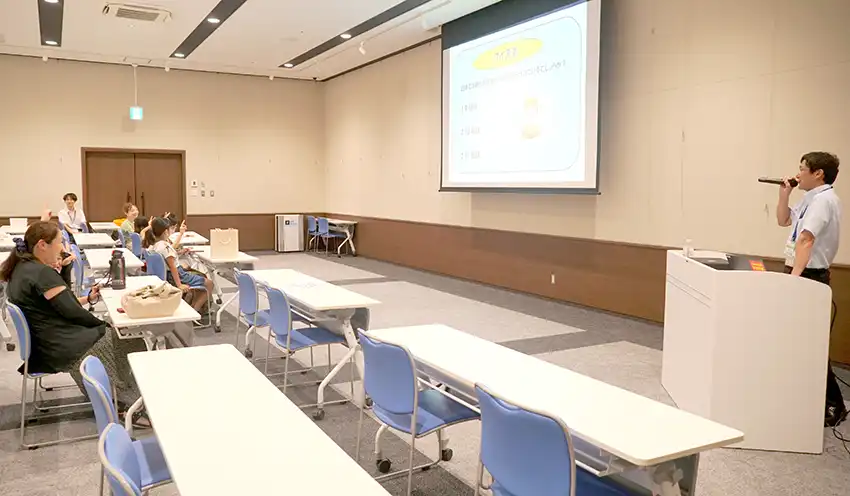 お金に関するクイズを出す笠原次長（右、8月9日、イオンモール川口）