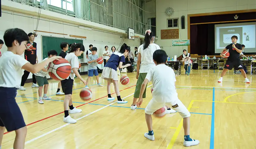 岡本選手（右）の指導でドリブル練習する子供たち（8月8日、越中島小学校体育館）