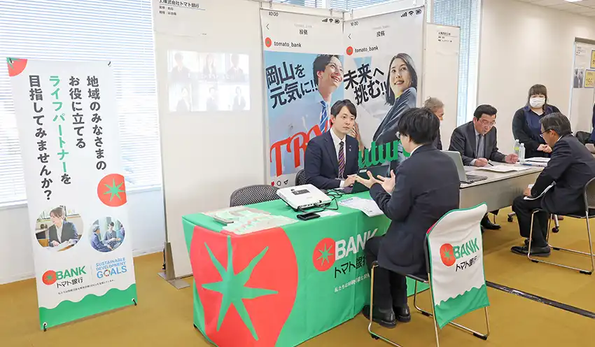 ジンジブのイベントで、高校教員に対して銀行業務や福利厚生制度を説明した越智部長代理（左、2月13日、山陽新聞本社ビル）