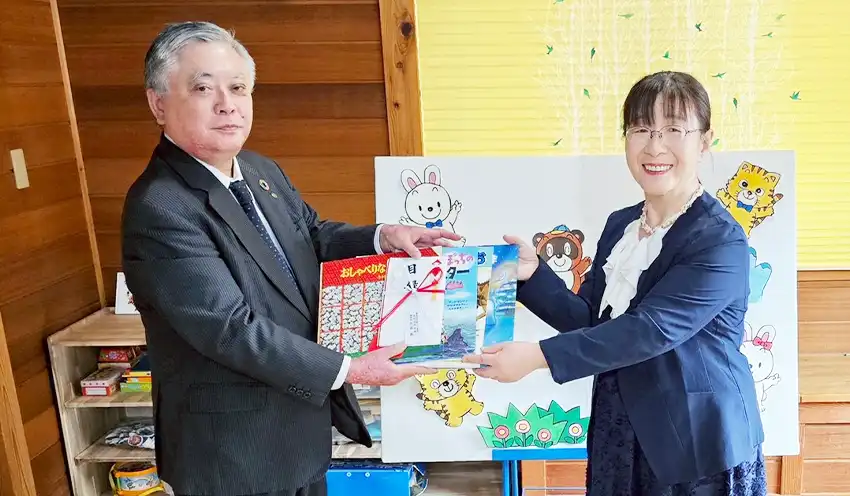 礪波理事長へ絵本を手渡す永岩理事長（左、3月26日、ほしの子、高岡信金提供）