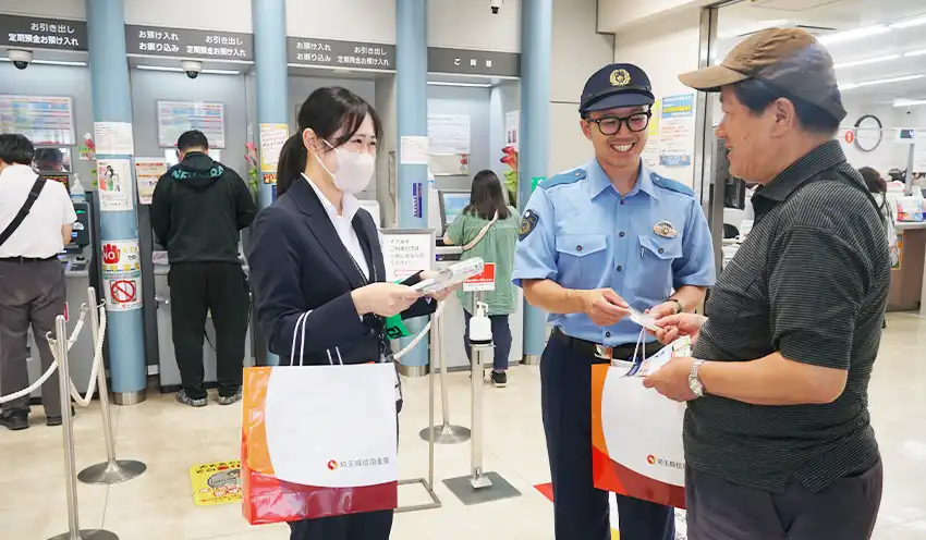 チラシを配布する埼玉県信金新入職員の諸井陽奈さん（左）と草加警察署の矢吹悠一郎巡査（中央、6月13日、同信金草加支店）