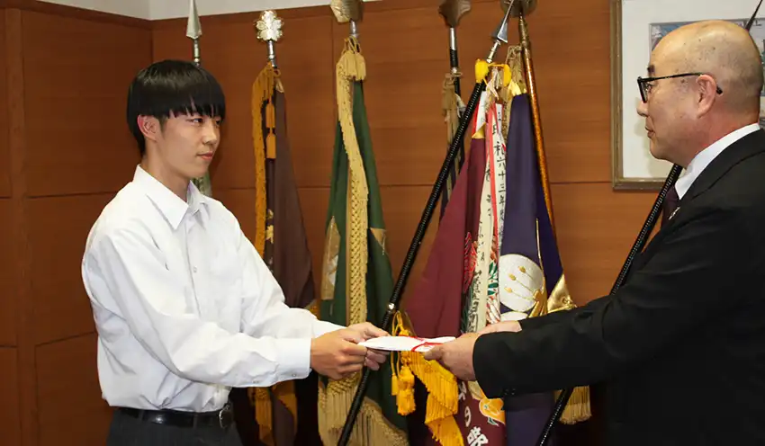 笛吹高校の農業クラブ副会長(左)に寄付目録を手渡す今福理事長(5月20日、笛吹高校、山梨県信農連提供)
