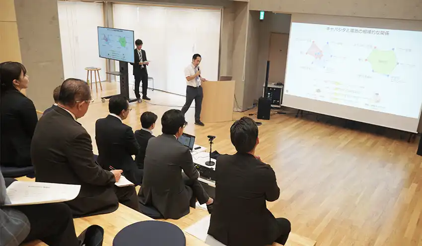 キャパシタの研究例を紹介する同大大学院の岩間悦郎准教授(奥左から2人目、6月13日、西東京国際イノベーション共創拠点)
