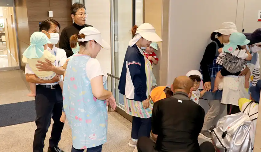園児を抱え階段で5階まで上る男性信金職員（左、7月15日、本店）