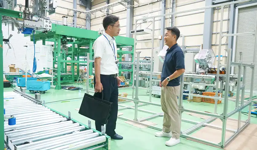 オーロラ会の会員で合理化装置・省力化機械の製造を手掛けるマカベの眞壁宏仁代表取締役（右）に新工場について情報交換する森内支店長（2025年７月22日、マカベ工場）