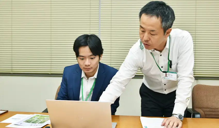 シン・カイジュンさんに経営企画部の業務を説明する西村・広報室長（右、7月24日、本店）