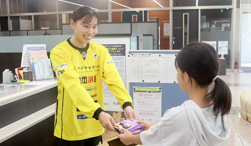 小学生(右)から古着を受け取る片山選手(8月18日、本店営業部、甲府信金提供)