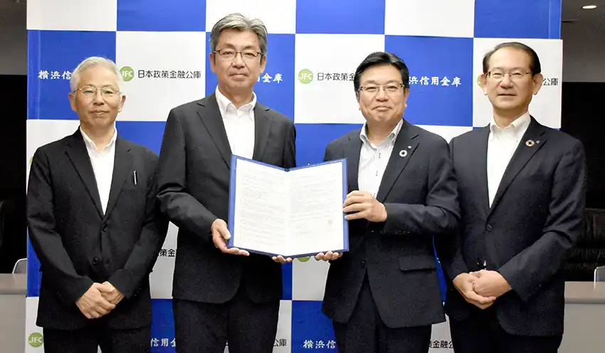 覚書を掲げる佐藤支店長(左から2人目)と春日理事長(左から3人目、8月26日、横浜信金本店)