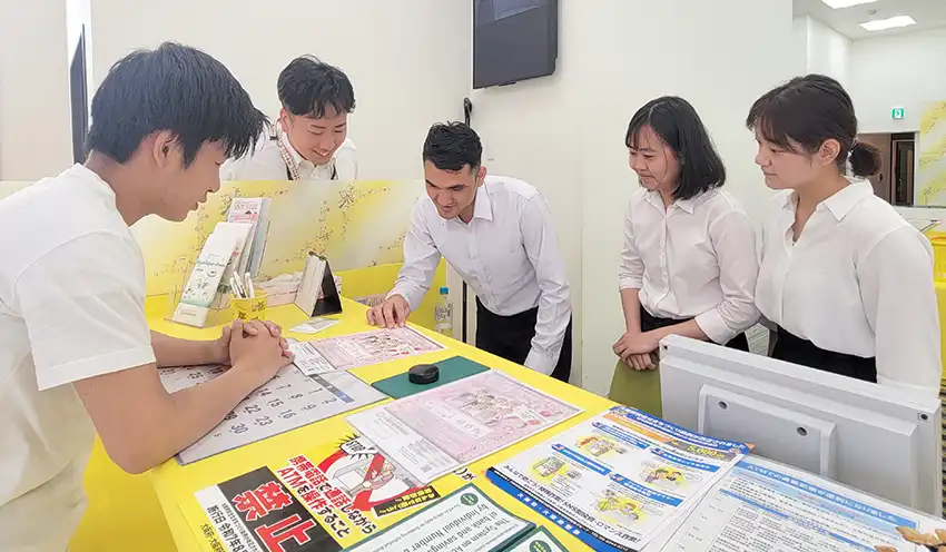 職員（左の2人）から窓口業務の指導を受けるインターン生3人（右の3人、8月28日、本店）