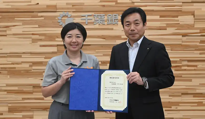 宇井代表取締役に助成金を交付する山﨑取締役専務執行役員（右、8月20日、本店）