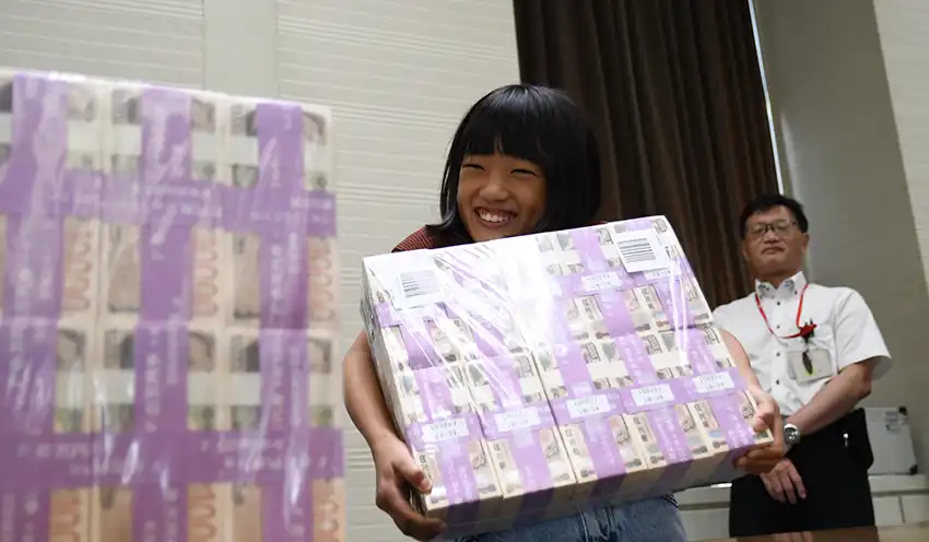 現金1億円を持ち上げる小学生(8月20日、本店)