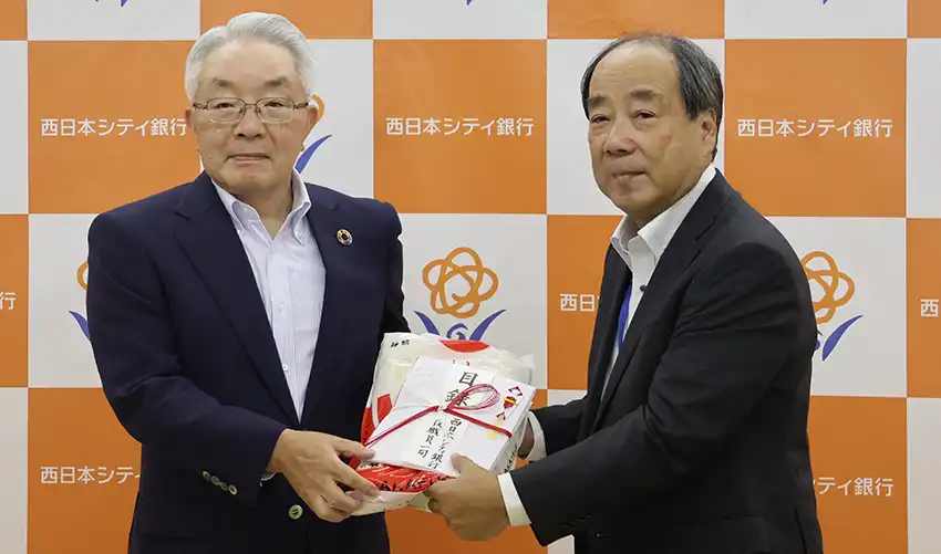 フードバンク福岡の岩﨑氏にコメを手渡す村上頭取（左、8月6日、本店別館）