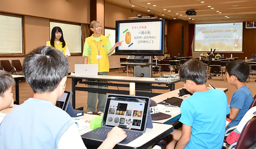 児童にお金の歴史について解説する福島高専の生徒（中央奥、8月7日、東邦銀本店）