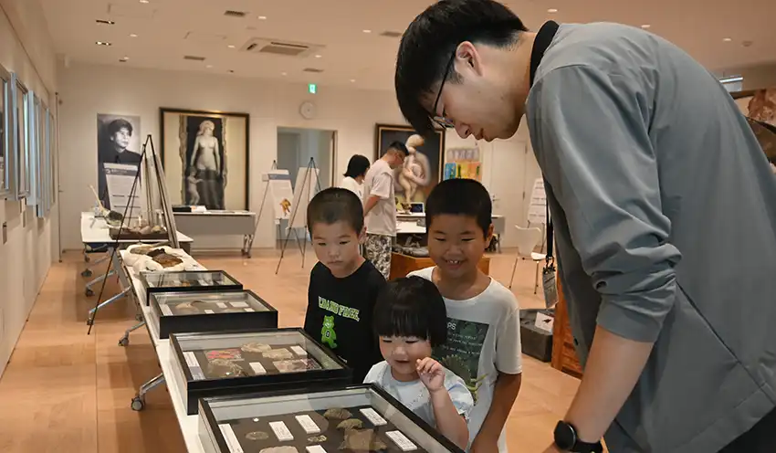 展示された化石を鑑賞する子供たちと長崎市恐竜博物館学芸員の小平将大さん（右、8月2日、あぶくま信金本店）