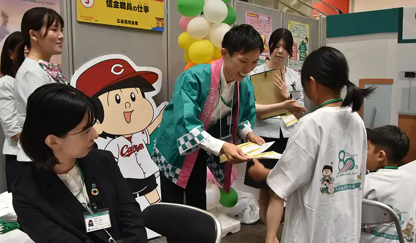 広島信金職員（中央）から給与明細を受け取る参加者（8月24日、イオンモール広島府中）