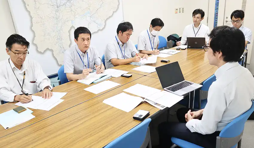 県職員や櫻林室長代理（右から3人目）らに事業案を話す伊藤代表（右、8月7日、山梨県庁）