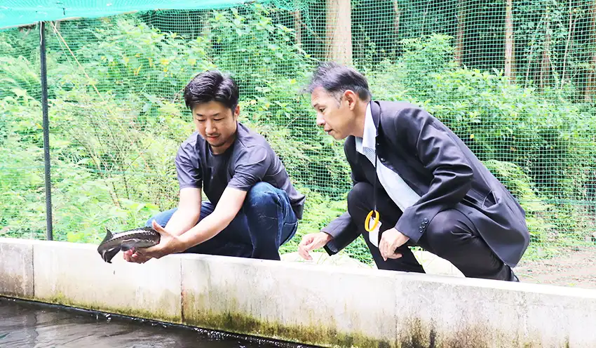 チョウザメの稚魚を見せる米丸さん（左）と小玉副支店長（9月12日、宮崎県日南市）