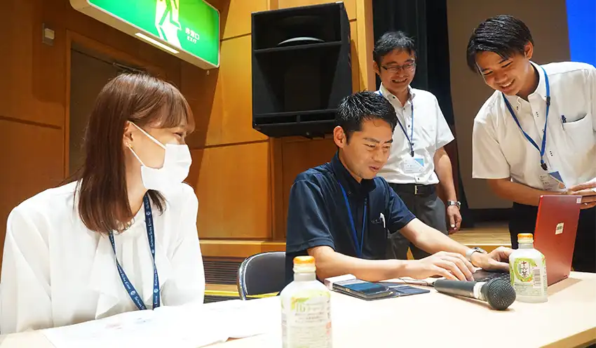 中高生向けの金融教育の教材を確認する宮島氏（中央、25年8月8日、埼玉県所沢市の富岡まちづくりセンター）