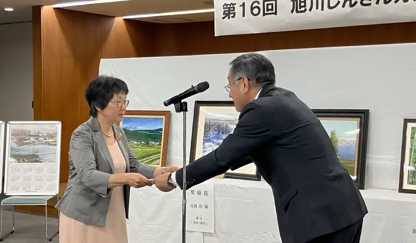 大賞に選ばれた菊池さん（左）に表彰状を手渡す武田理事長（9月3日、旭川信金本店）