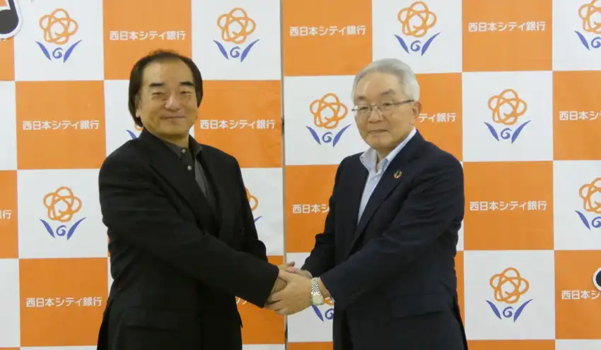 握手する井﨑氏（左）と村上頭取（9月26日、西日本シティ銀本店別館）