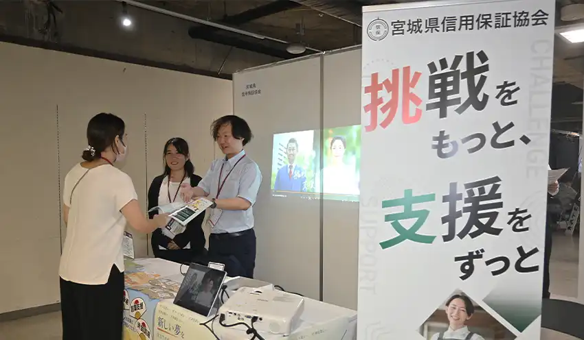 ブースで来場者に支援内容を説明する宮城県信保協の職員ら（右、9月26日、仙台市）