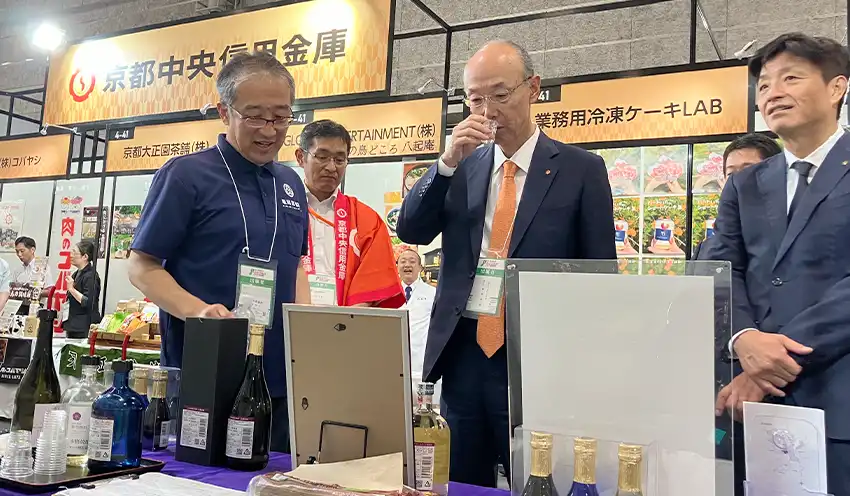 専用エリアに出展した取引先の展示品を試飲する植村理事長（中央、9月5日、インテックス大阪）