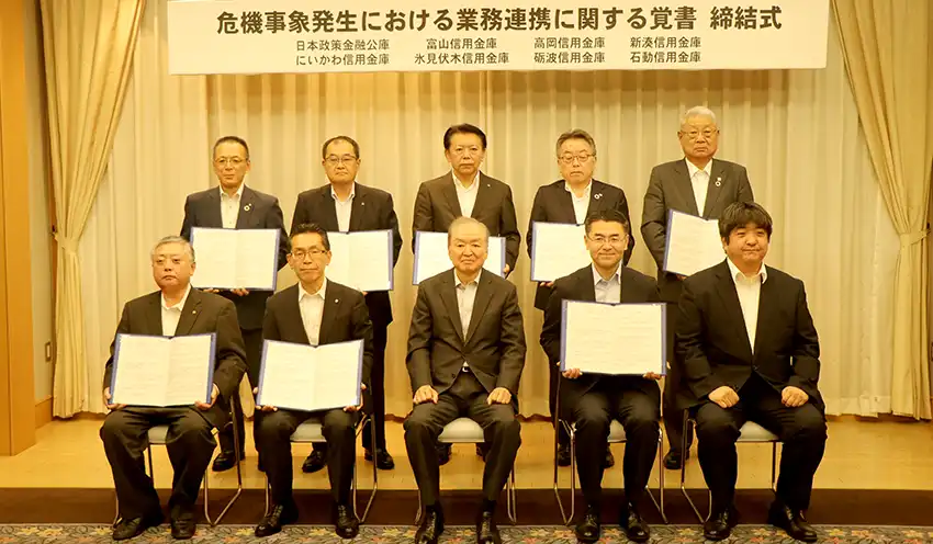 覚書を結ぶ関係者たち。前列左から3人目が山地会長、同4人目が五十嵐支店長（10月20日、高志会館）
