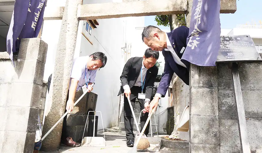 店舗敷地内の一角に祀られた須崎八幡の清掃に精を出す（左から）八幡浜事務所の前田將弥課長と日林伊織さん、小路支店長（10月21日）