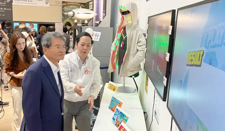 最適な温度を自動調節する服について説明を受ける髙井理事長（左、10月7日、リボーンチャレンジ）