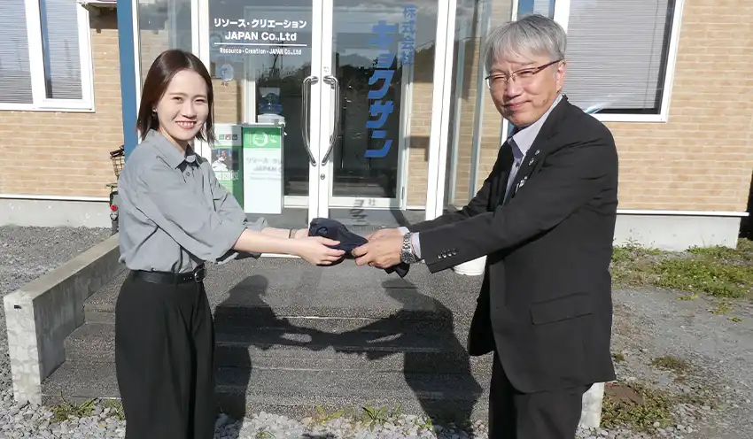 不要になった制服をキョクサンの社員（左）に手渡す職員（10月15日、キョクサン本社工場、北空知信金提供）