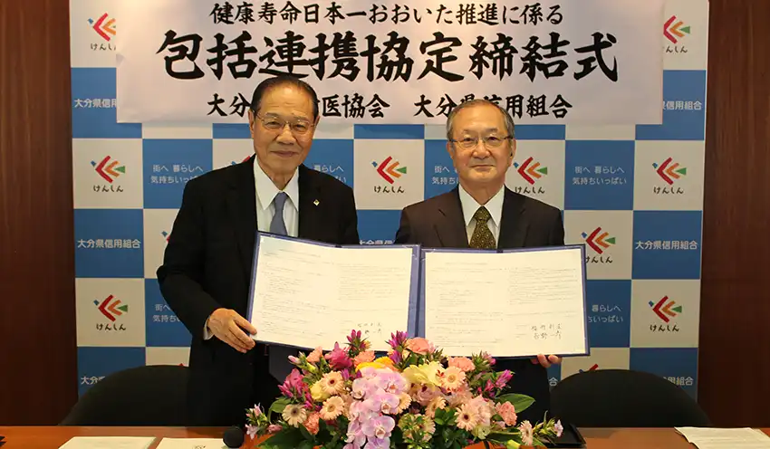 協定書を掲げる（左から）𠮷野理事長と福井会長（10月2日、本店、大分県信組提供）