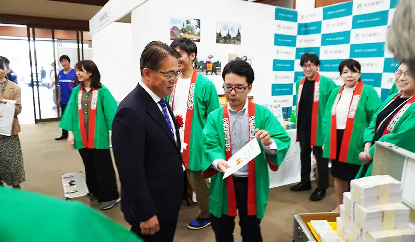 名古屋銀のブースでタイと日本の物価クイズに答える大村知事（左、10月11日、名古屋市）