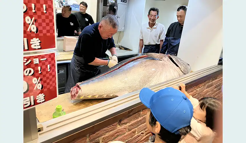 マグロの解体にくぎ付けになる子どもら(手前、10月11日、渡島信金札幌支店併設のアンテナショップ・みなほっの杜)