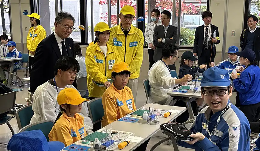 ミニカーの燃料電池組み立てを見守る上條理事長（左奥から4人目）と佐竹常務（同6人目、11月1日、中央台公民館）